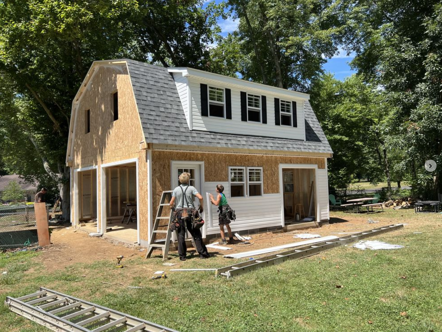 Crew assembling a two-story barn on-site — siding being installed with exposed OSB framing